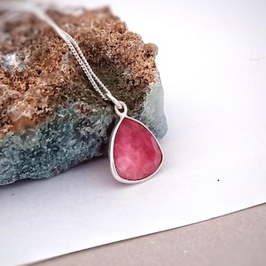 Op de afbeelding: Een zilveren ketting met een traanvormige hanger met een roze edelsteen.