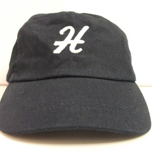 Può includere: Un cappello da baseball nero con una lettera "H" ricamata in bianco sul davanti.
