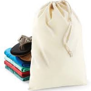 May include: An off-white drawstring bag is positioned next to a stack of folded towels in shades of blue, red, and green. A pair of black and brown sandals sits atop the towels, suggesting a holiday or travel theme.