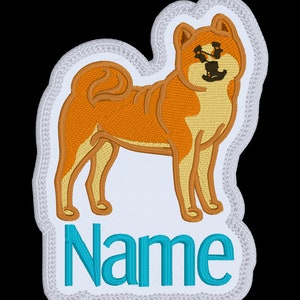 May include: White embroidered patch featuring a brown and cream Shiba Inu dog standing on a white background. The text "Name" is embroidered in turquoise below the dog.