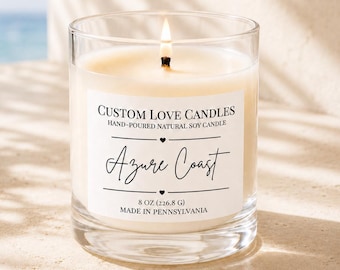 May include: A clear glass jar candle with a lit wick and white wax. The label reads: CUSTOM LOVE CANDLES, HAND-POURED NATURAL SOY CANDLE, Azure Coast, 8 OZ (226.8 G), MADE IN PENNSYLVANIA. The candle features a simple, clean design.