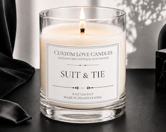 May include: A clear glass candle with a white label reading Custom Love Candles, Suit & Tie, 8 oz (226.8 g), Made in Pennsylvania. The candle contains off-white wax with a single lit wick, positioned in front of a black suit jacket.