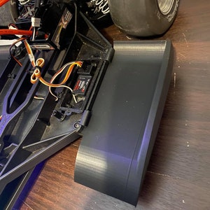 May include: A black plastic body panel for a remote control car. The panel is curved and has a smooth, glossy finish.