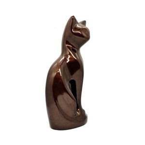 May include: A brown ceramic cat figurine in a sitting position. The cat is looking to the right. The figurine has a glossy finish.