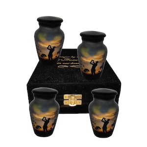 Könnte beinhalten: Satz von vier schwarzen und goldenen Urnen mit einem Golfer-Silhouetten-Design. Die Urnen werden auf einer schwarzen Samtbox mit einem goldenen Verschluss präsentiert. Die Urnen sind etwa 10 cm hoch.