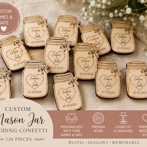 May include: A collection of small, light-colored wooden cutouts shaped like mason jars. Each piece features an engraved heart containing the text Emma & Josh and the date 07.19.2025. The jars include a small bow detail on the side of the lid.