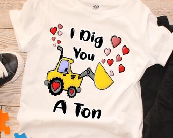 May include: White t-shirt with a colorful graphic. The design features a yellow construction vehicle with a heart on the wheel, the text "I Dig You A Ton", and floating hearts in red and pink.