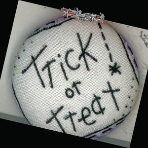 May include: White fabric button with black embroidery that reads "Trick or Treat!" with a star.