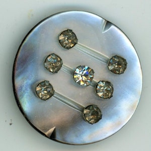May include: A round, iridescent, mother-of-pearl button with a silver-toned metal frame and seven clear rhinestones.