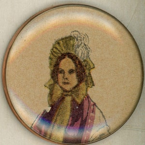 May include: A vintage glass button with a printed image of a young girl wearing a white bonnet and a purple dress.