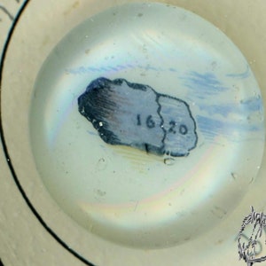 May include: A close-up of a small, round, glass paperweight with a blue and white image of a small island with the text "16.20" on it.