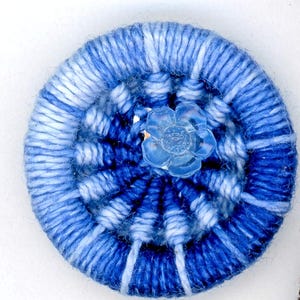 May include: A blue and white yarn button with a clear plastic flower in the center.