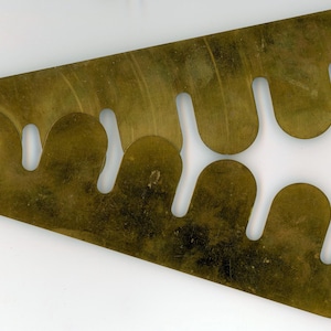 May include: A brass tool with a series of wavy, cut-out shapes. The tool has a small hole in the top left corner.