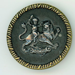 May include: A silver-toned metal button with a raised design of a child riding a lion. The button has a gold-toned metal rim with a rope-like design.