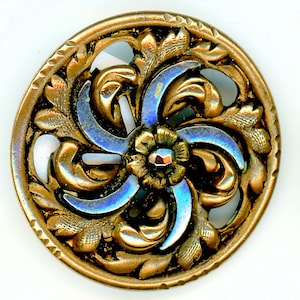 May include: A round, metallic button featuring an intricate openwork design of swirling leaves and a central flower. The metal has a warm, aged bronze finish with iridescent blue highlights on the curved petals, and a notched outer rim.