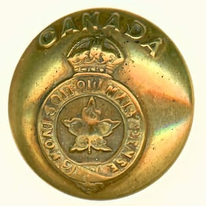 May include: A gold-colored metal button with the words "CANADA" and "SOIT QUI MAL Y PENSE" surrounding a maple leaf and a crown.