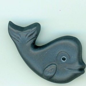 May include: A dark gray whale figurine with a smiling face, eye, and fin details. The whale is a solid color and has a smooth texture. The figurine is a decorative item.