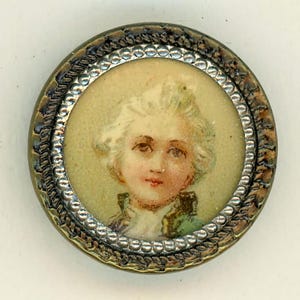 May include: A round, silver-toned button with a raised, beaded border. The button features a painted portrait of a young person with white hair, wearing a green and white jacket.