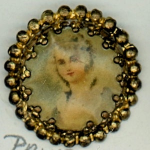 May include: A small, round antique brooch with a portrait of a woman. The portrait is surrounded by a gold-colored beaded frame. The woman in the portrait has light skin and is wearing a white dress.