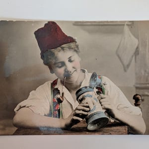 Cartolina fotografica reale di una donna in costume popolare con pipa e boccale di birra, colorata a mano, Norvegia 1907, RPPC d'epoca umoristica