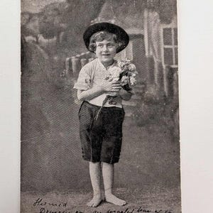 Menino de cartão postal vintage com flores, descalço e sorrindo, início dos anos 1900, enviado pela Dinamarca, cena de vila encantadora RPPC