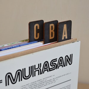 May include: A close-up of a vinyl record album with the title "MUKASAN" printed in black and white. The album cover features a black and white design with a circular record in the background. The album is labelled with the text "DOS-MUKASAN" and includes a list of song titles in Russian and English.