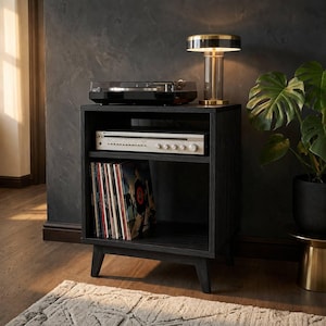 Puede incluir: Un mueble multimedia de madera negra con cuatro patas c&oacute;nicas, que cuenta con un estante superior abierto con un tocadiscos negro, un estante central con un receptor plateado y un estante inferior con una colecci&oacute;n de vinilos.