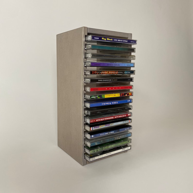 Peut inclure: Une tour de rangement en bois gris pour CD avec 18 fentes pour CD. La tour est remplie de CD avec diff&eacute;rents titres et artistes.
