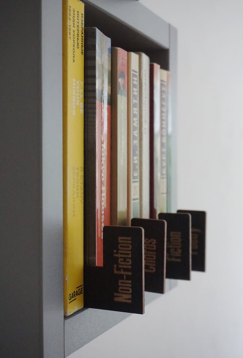 Puede incluir: Una estanter&iacute;a con una variedad de libros, organizados por g&eacute;nero. Los g&eacute;neros est&aacute;n etiquetados con etiquetas de madera: No ficci&oacute;n, Acordes, Ficci&oacute;n y Poes&iacute;a.