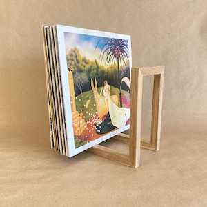 May include: A wooden record stand holding a stack of vinyl records. The record cover shows a painting of a woman and a white animal in a woodland scene. The record is titled "Through the Looking Glass" by "Mood Swings".