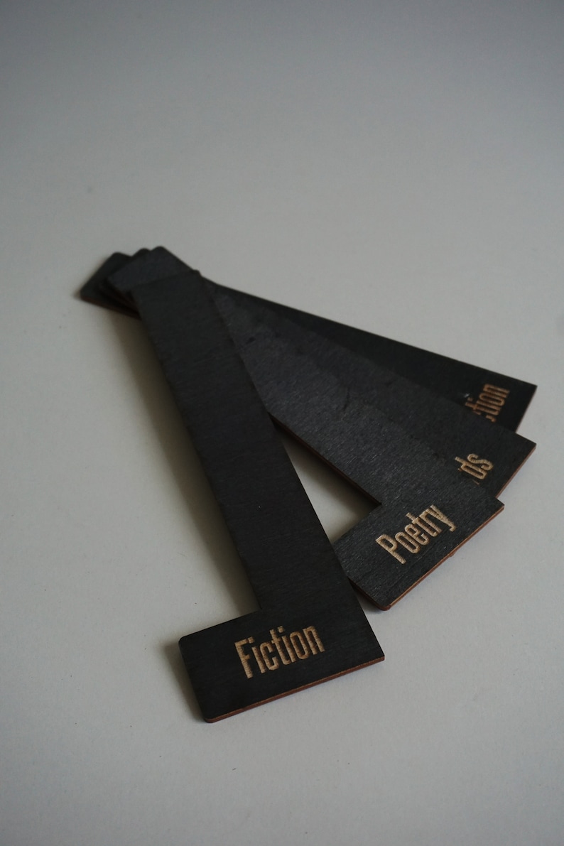 Puede incluir: Tres sujetalibros de madera negra con las palabras "Fiction", "Poetry" y "Fiction" escritas en letras doradas.