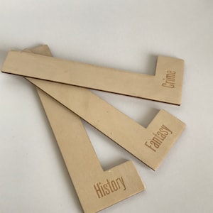 Puede incluir: Tres sujetalibros de madera con las palabras "Historia", "Fantas&iacute;a" y "Crimen" grabadas en ellos.
