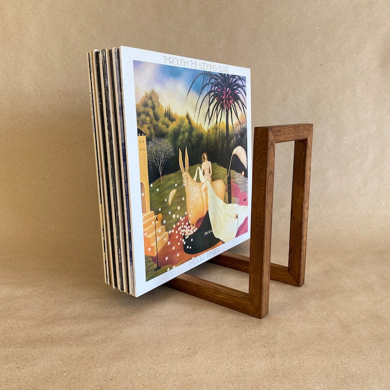 May include: A wooden record stand holding a stack of vinyl records. The record cover shows a painting of a woman riding a white donkey in a woodland scene. The album title is "Through the Looking Glass" by "Mike Oldfield".