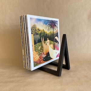 Peut inclure: Un support à disques en bois foncé de forme triangulaire, sur lequel est posé un empilement de disques vinyles. Le disque du dessus est intitulé "Through the Looking Glass" par "Moriarty".
