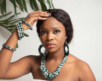 May include: A set of fabric jewelry featuring a chunky knotted necklace, large circular hoop earrings, and three matching bangles. The pieces are crafted from a dark green and light pink striped textile material with a soft, wrapped appearance.