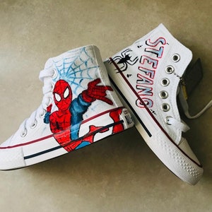 May include: White high-top sneakers with a hand-painted design featuring Spiderman, a web, and the name "STEFANG" on the other shoe.