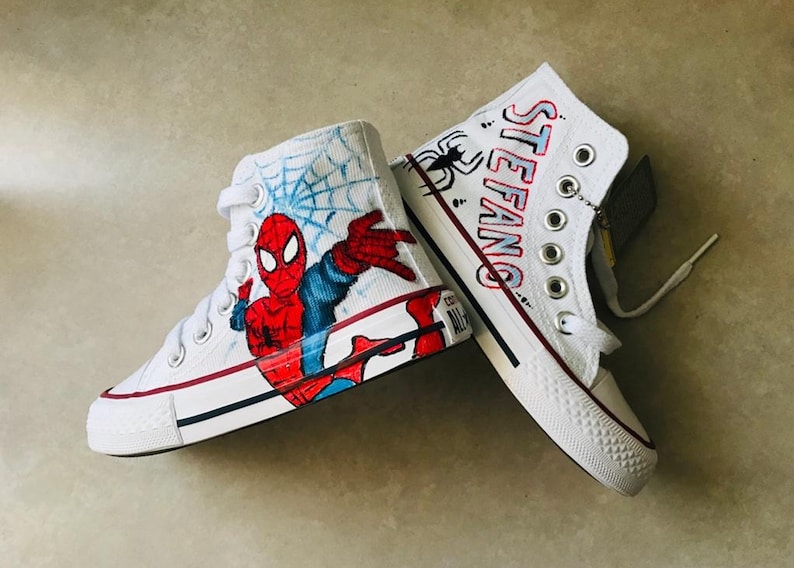 May include: White high-top sneakers with a hand-painted design featuring Spiderman, a web, and the name "STEFANG" on the other shoe.