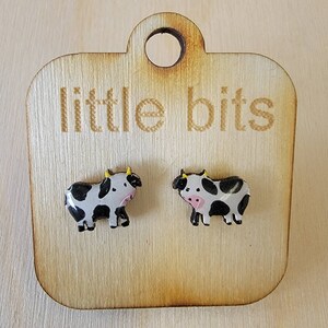 May include: A pair of black and white cow stud earrings on a wooden display card with the text "little bits".