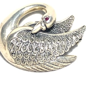 Puede incluir: Un broche de cisne de plata con un ojo de piedra roja y un diseño detallado de piedras de marcasita.