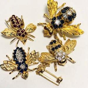 May include: Four gold bee brooches with ruby and sapphire accents. The brooches are detailed with intricate designs and feature a variety of gemstones.