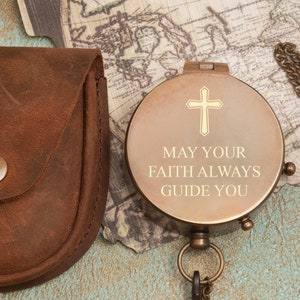 May include: A brass compass with a leather pouch and a chain. The compass face has the words "May your faith always guide you" engraved on it.