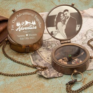 Pode incluir: Uma bússola de latão com uma corrente, com uma inscrição personalizada na tampa que diz "For Our Adventures Together Adventure Awaits Sammy Rhonda Feb 19th 2023". A tampa também tem uma foto de um casal.