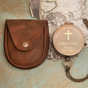 May include: A brass compass with a leather pouch. The compass face has the inscription "May your faith always guide you" with a cross and the name "John Craig" with the date "Baptized Sep 2, 2020".