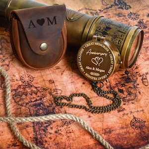 May include: A vintage-style brass telescope and compass set on a map background. The compass is engraved with "Anniversary" and a couple's names. A leather case with initials is also present.