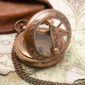 May include: A brass compass with a chain and a leather case. The compass has a clear face with a compass rose and numbers around the edge. The compass is open and the needle is pointing north.