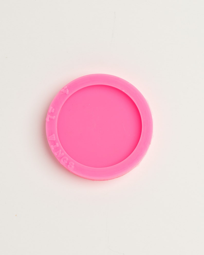 Peut inclure: Moule en silicone rose vif, de forme circulaire, avec le texte "7L Wings" en relief sur le bord ext&eacute;rieur. Le moule a un bord sur&eacute;lev&eacute; et un int&eacute;rieur lisse et plat. L'objet est probablement utilis&eacute; pour l'artisanat ou la p&acirc;tisserie.