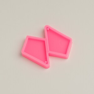 May include: Two bright pink, geometric-shaped silicone molds for crafting earrings. Each mold has a unique shape with a small hole for attaching earring hardware. The molds are designed for resin or other crafting materials.