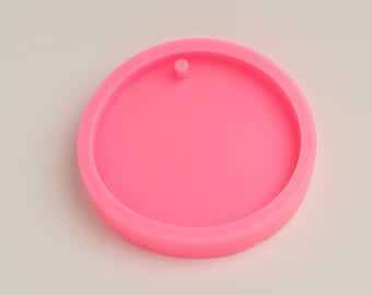 Op de afbeelding: Een felroze, cirkelvormige siliconen mal met een opstaande rand en een klein gaatje aan de bovenkant. De mal is ontworpen voor het knutselen en creëren van harskunst, sieraden of andere doe-het-zelfprojecten. Het gladde oppervlak is ideaal voor gemakkelijk loslaten.