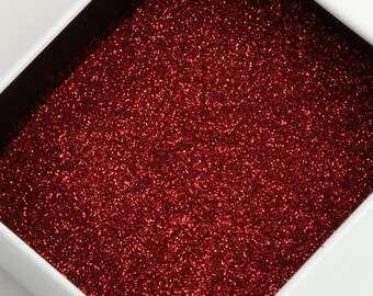 May include: A white, rectangular box filled with red glitter. The glitter sparkles, reflecting light. The box has a black interior and a white exterior, creating a contrast with the glitter.