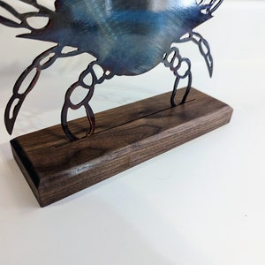 May include: A metal crab sculpture with a blue and brown patina, standing on a dark brown wooden base.